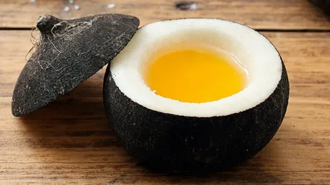 Nucă de cocos tânără deschisă, cu miezul alb și uleiul de cocos auriu vizibil în interior